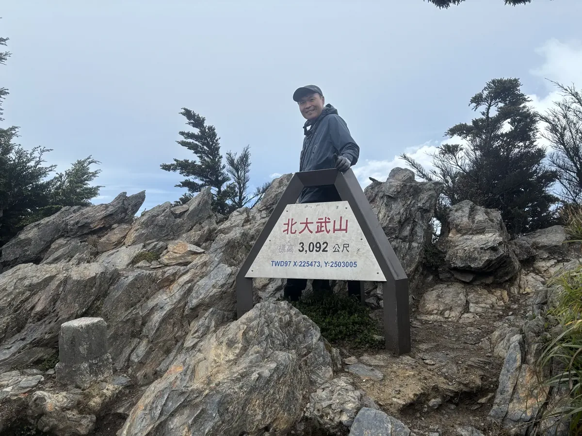 本人站在北大武山山頂標示牌後方,牌上寫標高 3,092 公尺,左下角是三角點基石